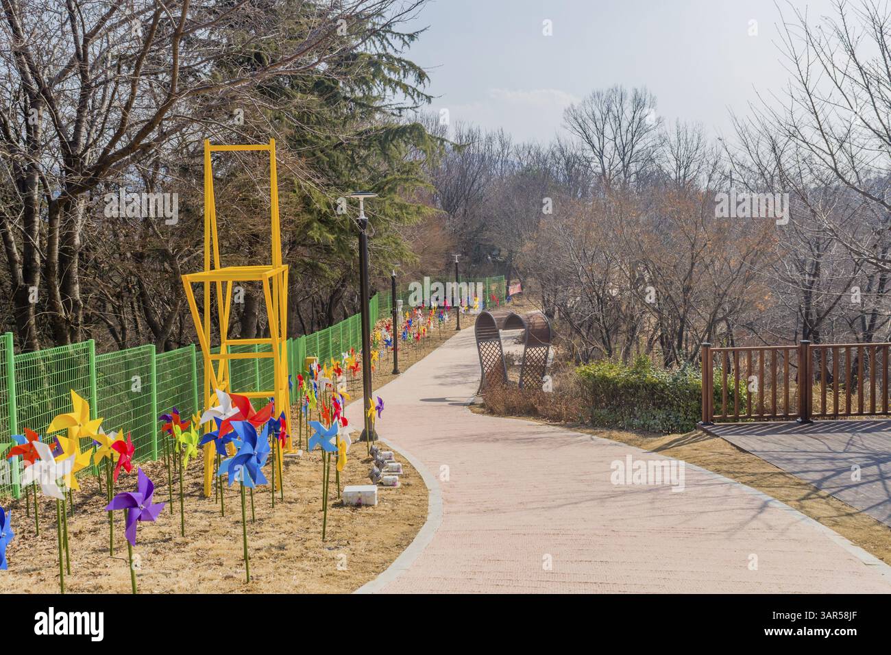 Un sentiero fiancheggiato da ruote a spillo colorate e da un'alta scultura gialla, circondato da alberi, Daejeon, Corea del Sud. 26 febbraio 2025 Foto Stock