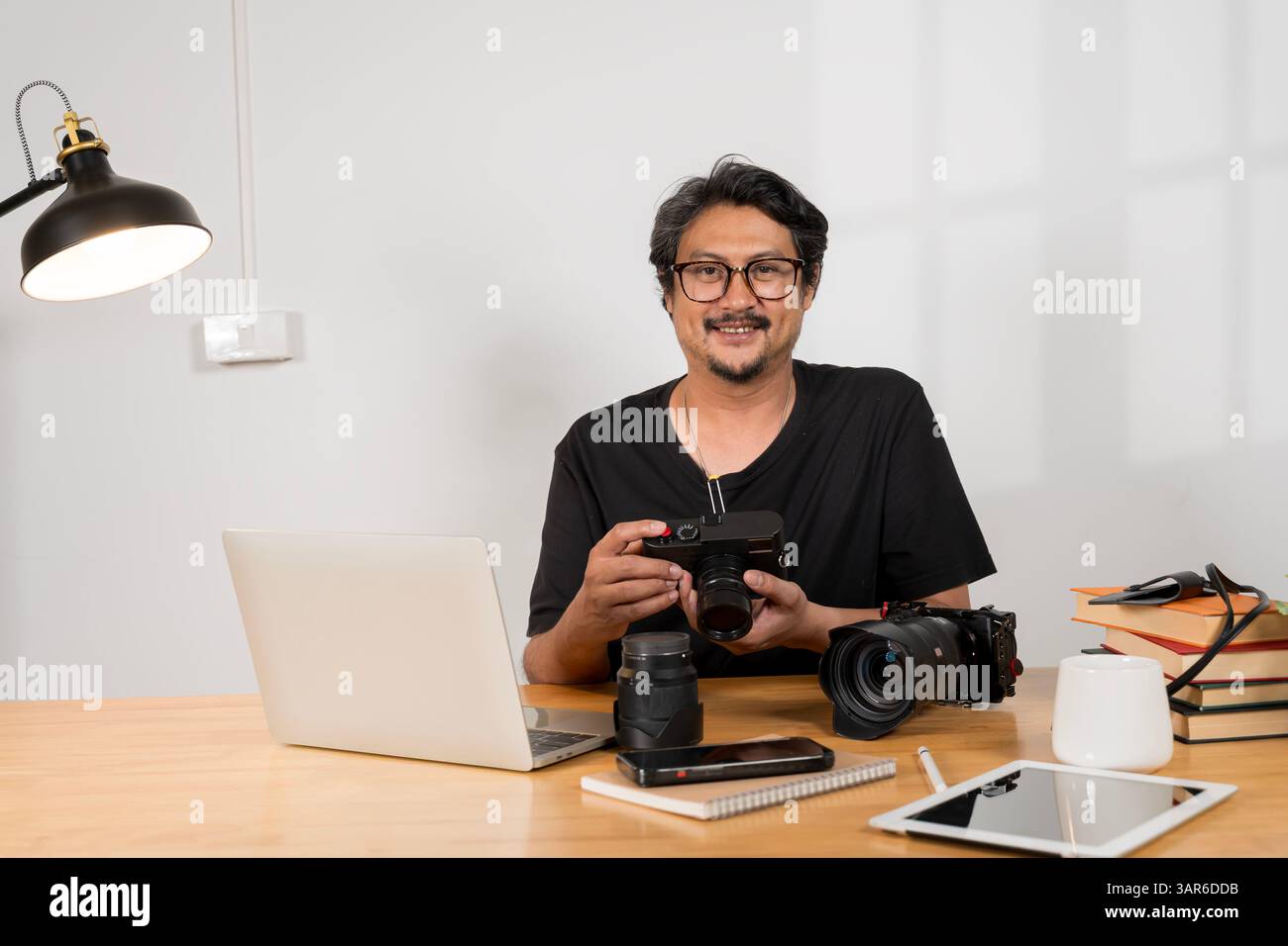 Ritratto di un attento fotografo con la barba seduto a fissare la fotocamera, schermo del computer alla scrivania, concetto di lavoro. Foto Stock