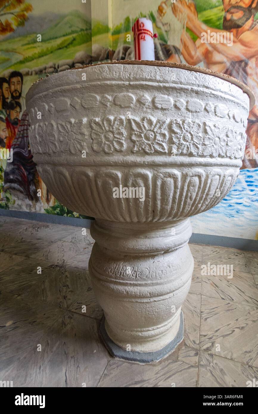 Un antico fonte battesimale in pietra con intricate incisioni all'interno della chiesa di Quipayo, una delle chiese più antiche di Bicol, nelle Filippine Foto Stock