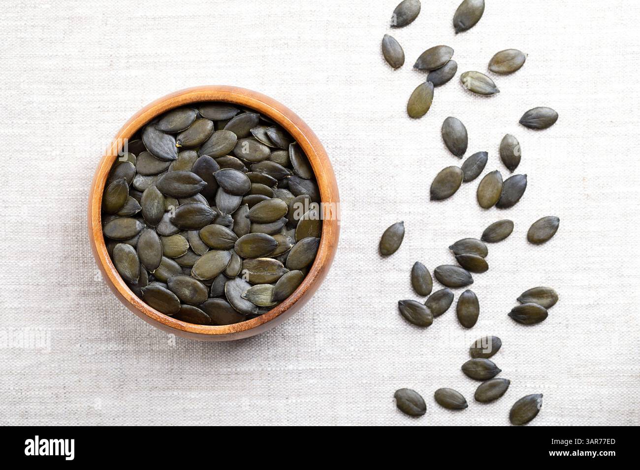 Semi di zucca con olio di Stiria in una ciotola di legno su lino. Frutta secca, verde scuro e frutta giovane della zucca della Stiria, Cucurbita pepo var. styriaca. Foto Stock