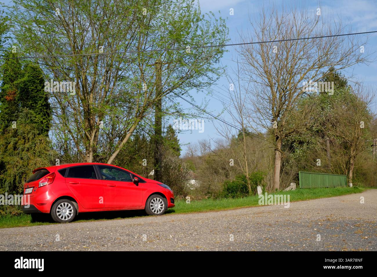 ford fiesta rosso brillante parcheggiato in una corsia rurale contrasta nettamente il cielo blu e il verde fogliame primaverile della contea di zala in ungheria Foto Stock