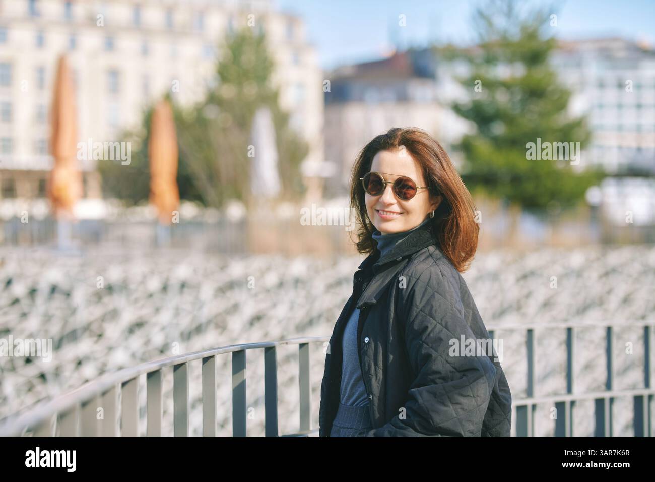 Ritratto all'aperto di una donna felice che indossa occhiali da sole e bomber nero, posa all'aperto Foto Stock