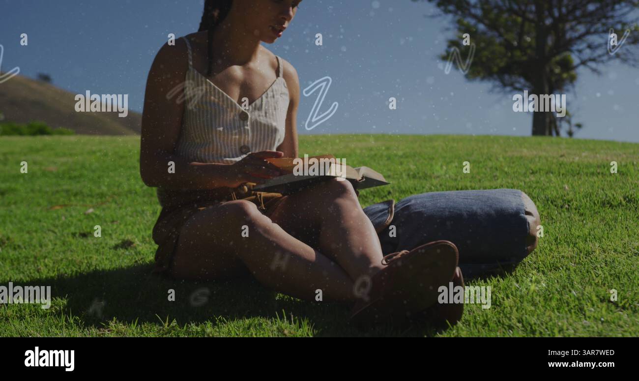 Diversi alfabeti fluttuano contro una donna afroamericana che legge un libro seduto sull'erba Foto Stock