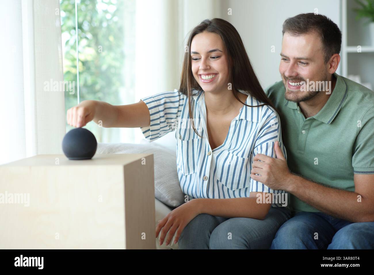 Coppia felice che inizia il nuovo altoparlante intelligente seduto sul divano di casa Foto Stock