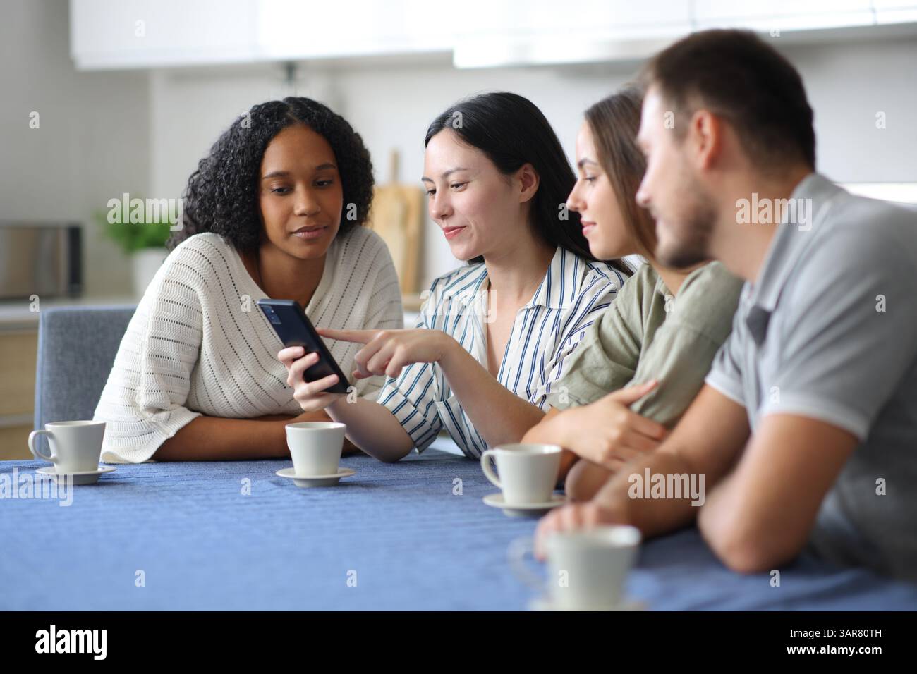 Amici interrazziali che usano lo smartphone in cucina a casa Foto Stock