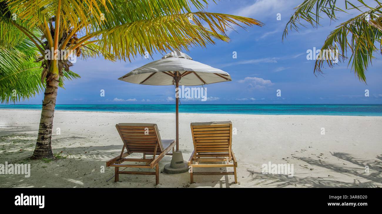 Rilassatevi con sedie a sdraio illuminate dal sole sotto l'ombrellone. Fuga romantica in luna di miele, paesaggio mozzafiato, vacanza tropicale panoramica. Primo piano sabbia marina cielo soleggiato Foto Stock