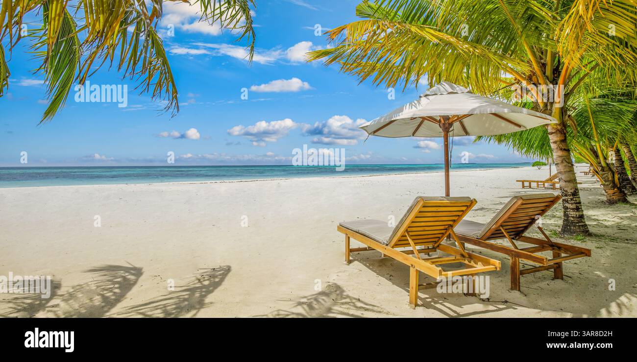 Rilassatevi con sedie a sdraio illuminate dal sole sotto l'ombrellone. Fuga romantica in luna di miele, paesaggio mozzafiato, vacanza tropicale panoramica. Primo piano sabbia marina cielo soleggiato Foto Stock