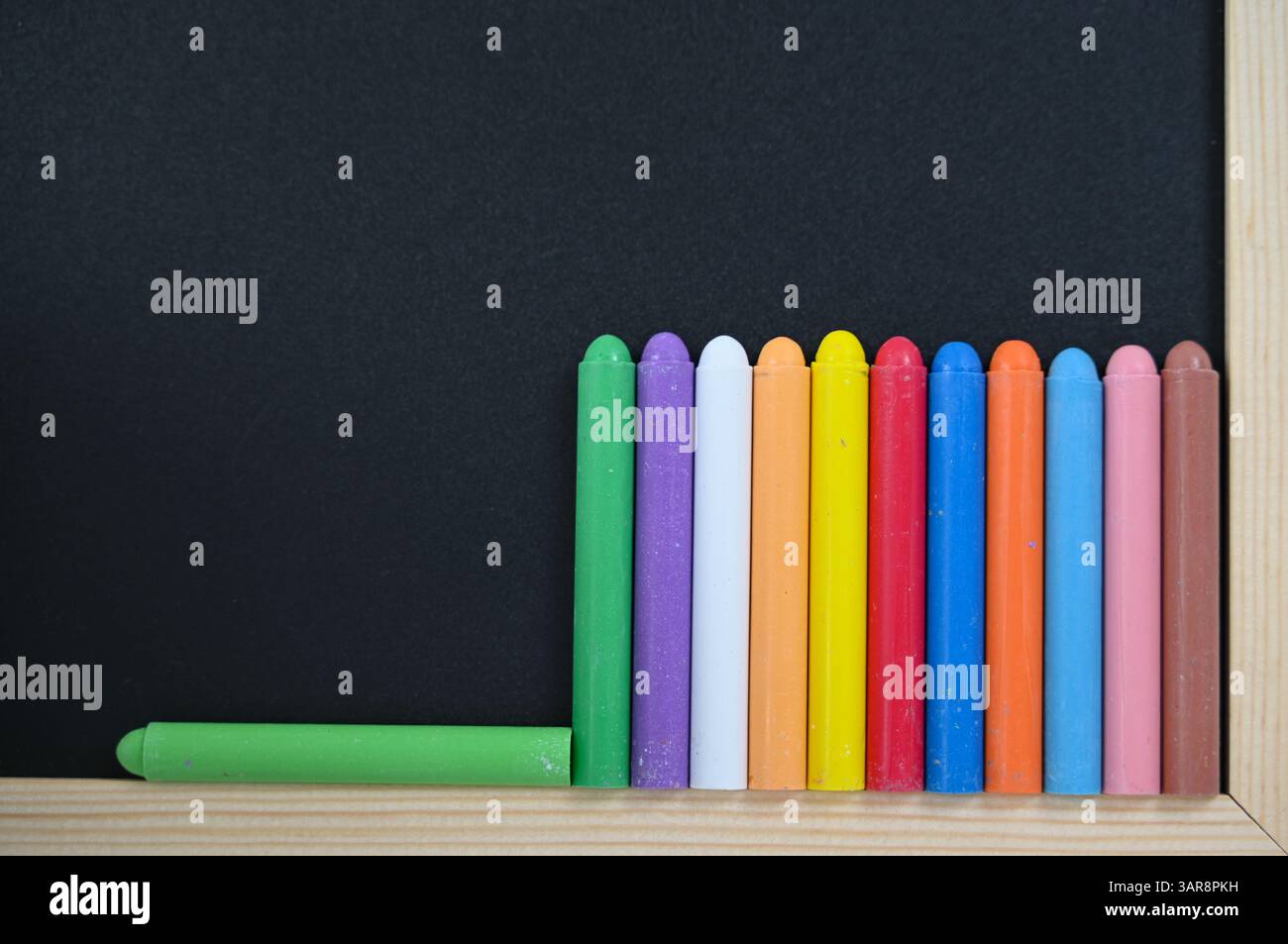 Una fila ordinata di pastelli colorati è disposta con cura e posizionata di fronte a una grande lavagna, pronta per le attività creative Foto Stock