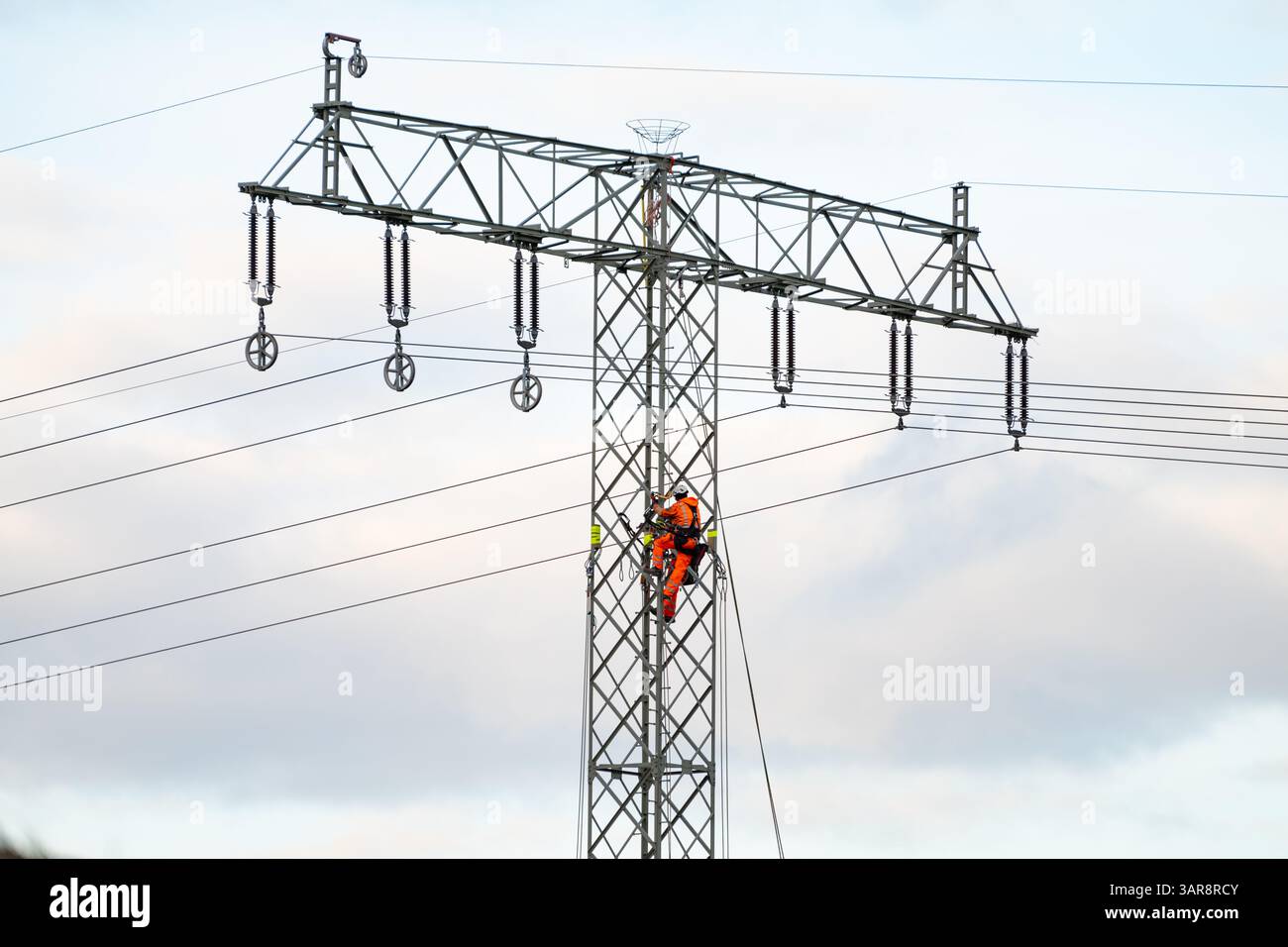 Scalatore industriale su un palo elettrico. Personale di manutenzione professionale del fornitore di energia elettrica. Luogo di lavoro per gli atleti con abbigliamento arancione. Foto Stock