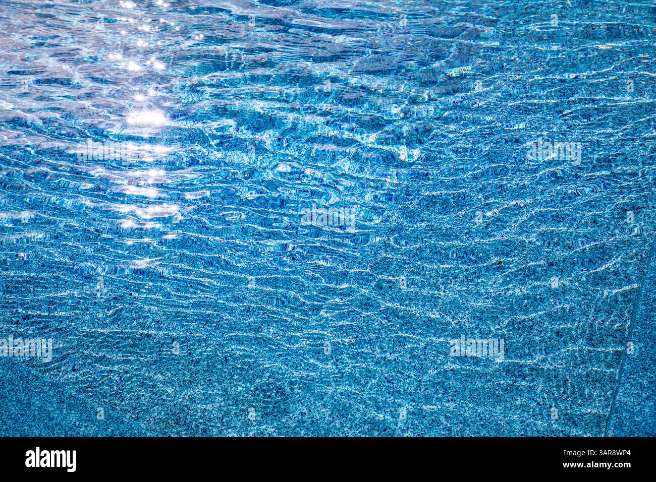 Vista ravvicinata dell'acqua astratta della piscina con luce estiva increspata, perfetta per sfondi di design e per rinfrescare l'atmosfera creativa dell'ispirazione tropicale Foto Stock
