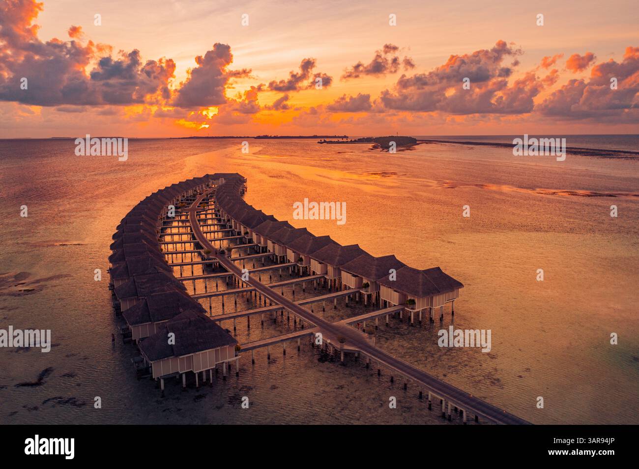 Vista aerea delle splendide ville sull'acqua delle Maldive durante un vibrante tramonto, con acque turchesi, paradiso tropicale e serene vibrazioni dell'isola Foto Stock