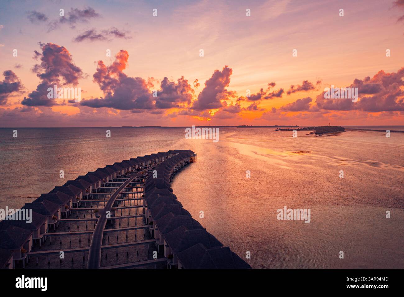 Vista aerea delle splendide ville sull'acqua delle Maldive durante un vibrante tramonto, con acque turchesi, paradiso tropicale e serene vibrazioni dell'isola Foto Stock