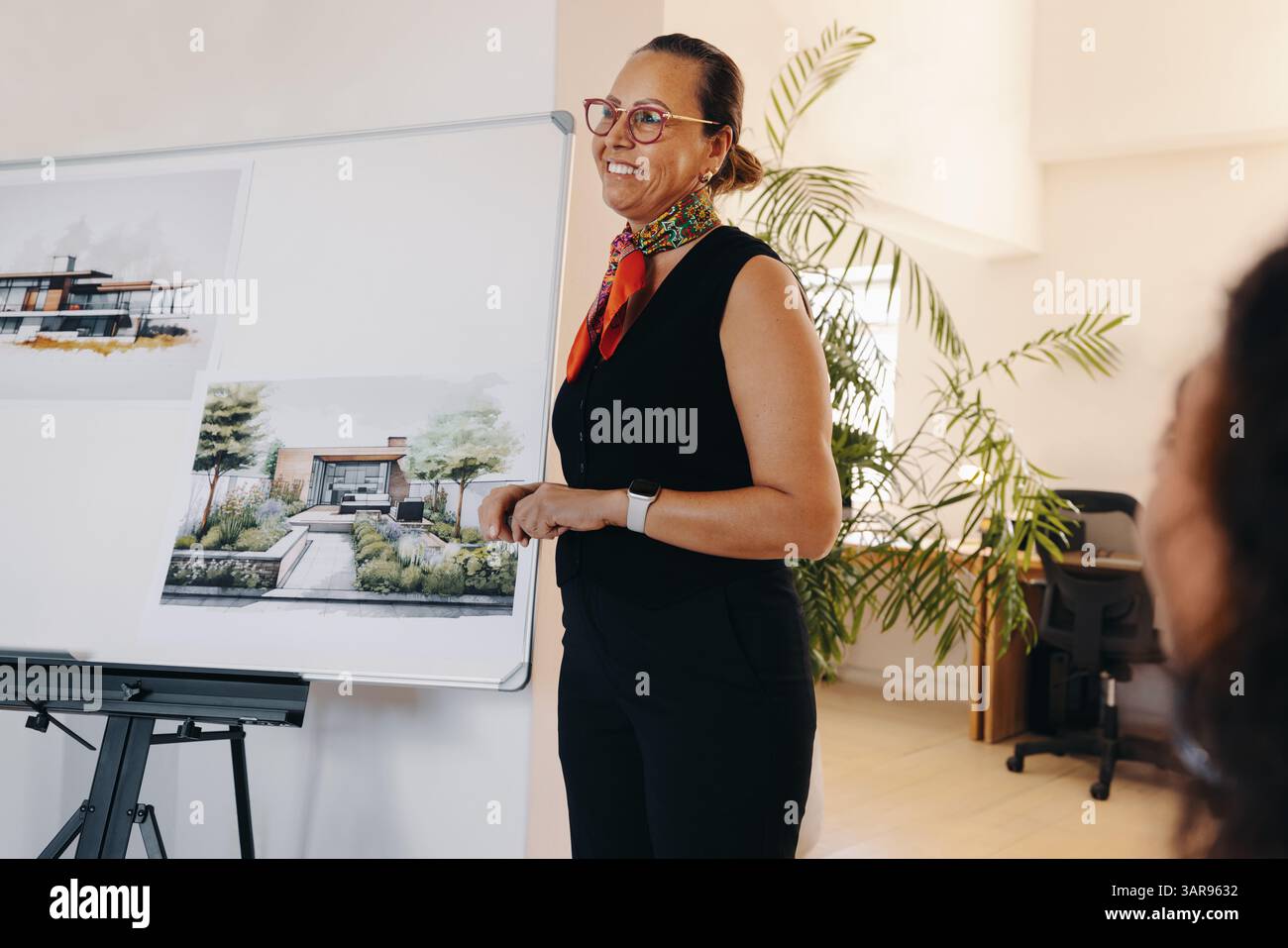 Una donna matura e sicura conduce una riunione di progetto, presentando progetti architettonici. Ispira le sue capacità di leadership, coinvolgendo i colleghi Foto Stock