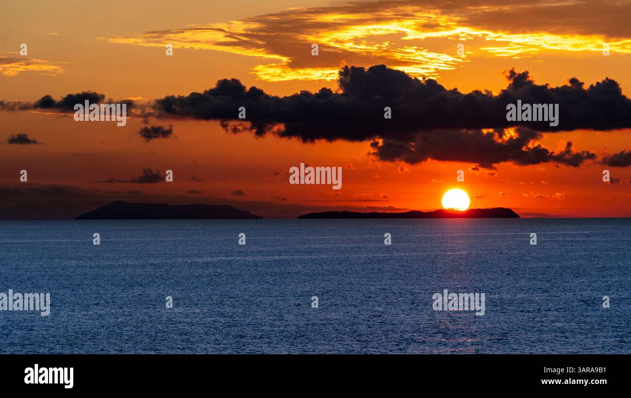Uno splendido tramonto sull'oceano, con il sole parzialmente nascosto dietro l'orizzonte. Il cielo è pieno di vivaci tonalità arancio e giallo, a contrasto Foto Stock