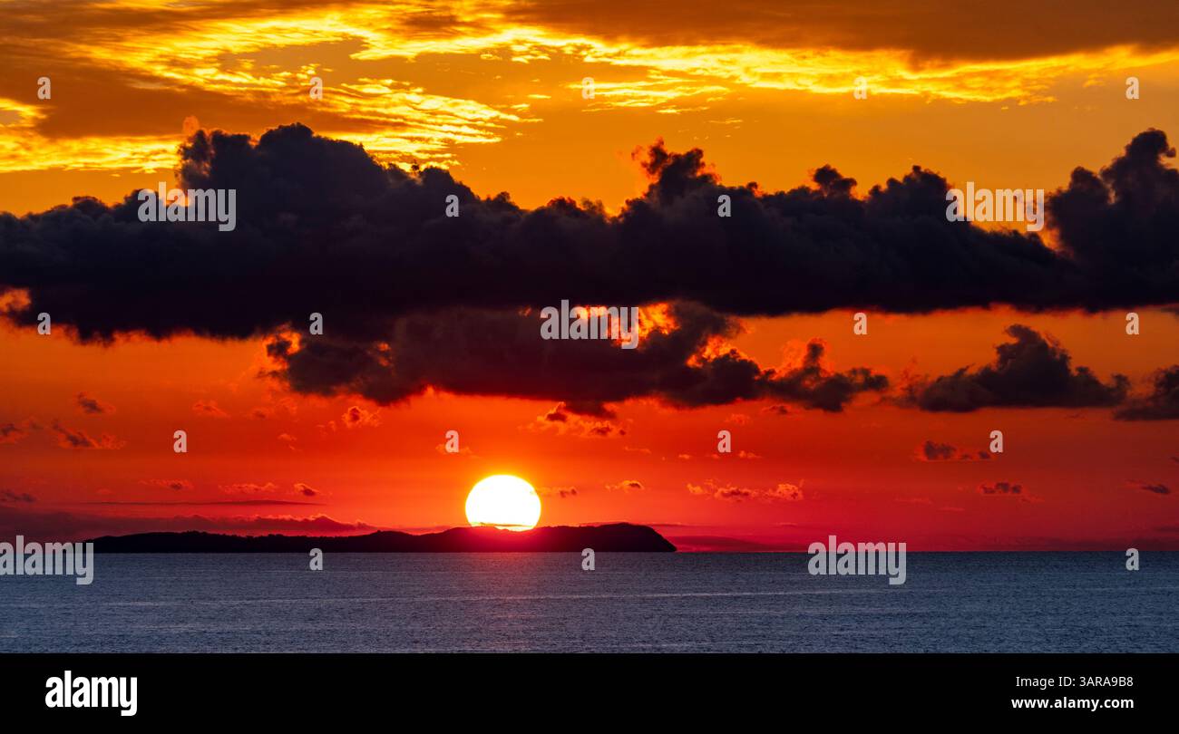 Uno splendido tramonto sull'oceano, con vivaci sfumature arancioni e gialle che illuminano il cielo. Mentre le nuvole scure contrastano con lo sfondo colorato Foto Stock
