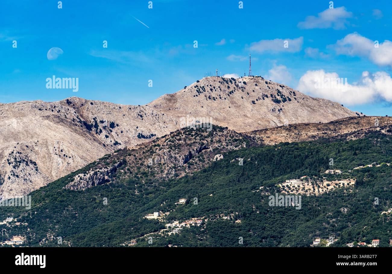 Una vista panoramica di un paesaggio montuoso caratterizzato da una cima rocciosa con torri di comunicazione in cima. Il primo piano mostra lussureggianti colline verdi e. Foto Stock