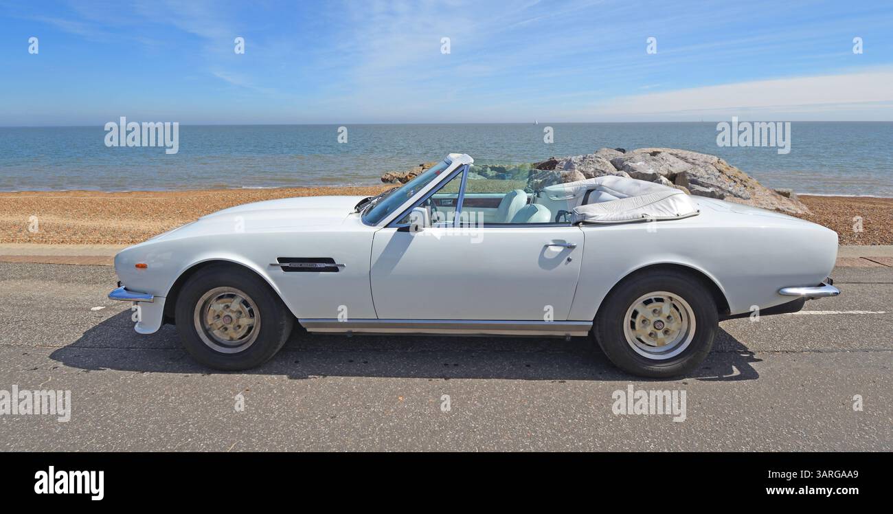Classic White Aston Martin V8 volante parcheggiata sulla spiaggia lungomare e sul mare sullo sfondo. Foto Stock