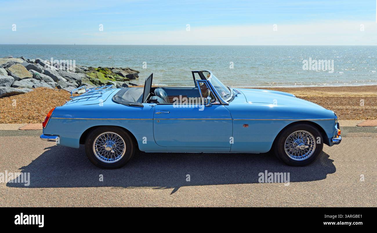 Classica Roadster MGB rifinita in Iris Blue parcheggiata sulla spiaggia di fronte al mare e sul mare sullo sfondo. Foto Stock