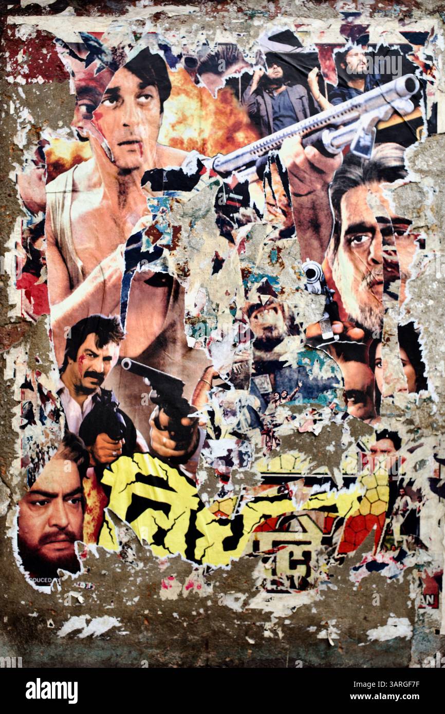 Poster del film d'azione di Bollywood sbiadito e lacerato su un muro di Delhi, la sua superficie stratificata rivela frammenti di pistole, fiamme ed espressioni eroiche. Foto Stock