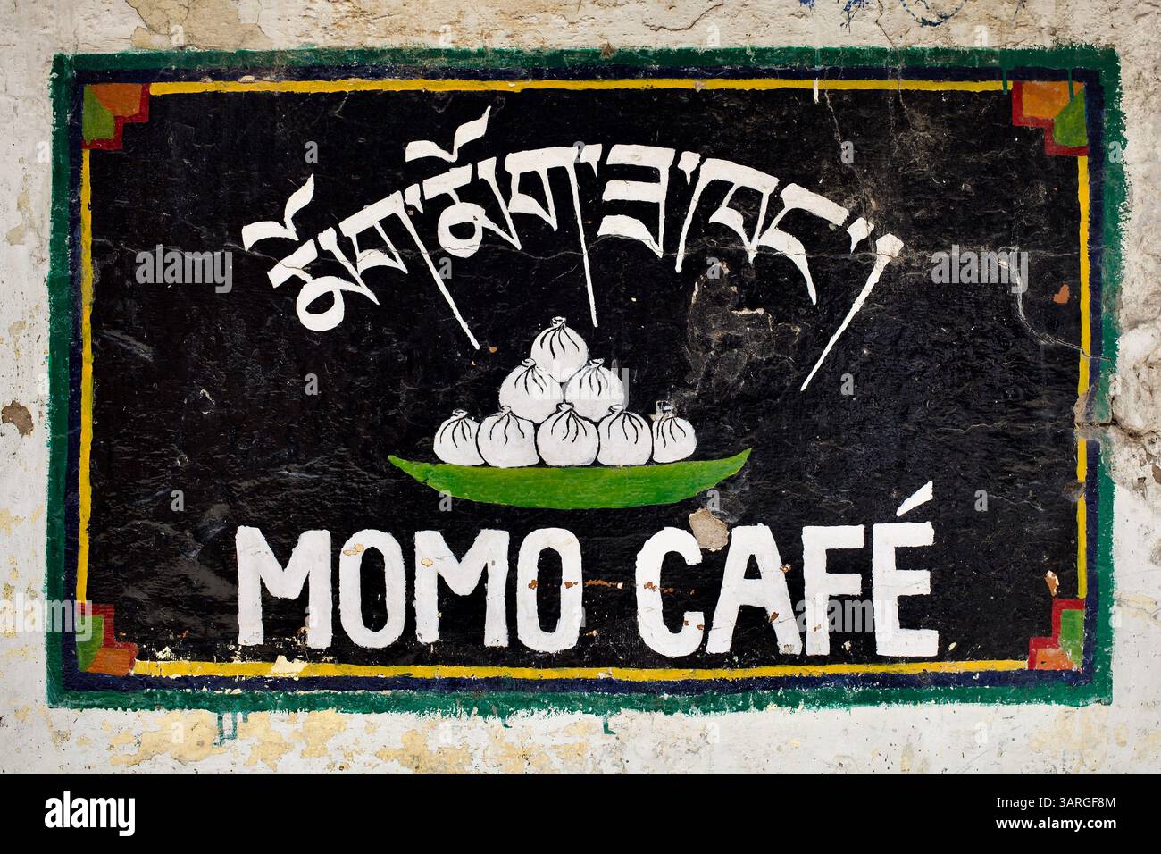 Insegna dipinta a mano per un Momo Café in stile tibetano a Dharamsala, con scritta tibetana e un piatto di gnocchi al vapore su un pannello a parete nero. Foto Stock