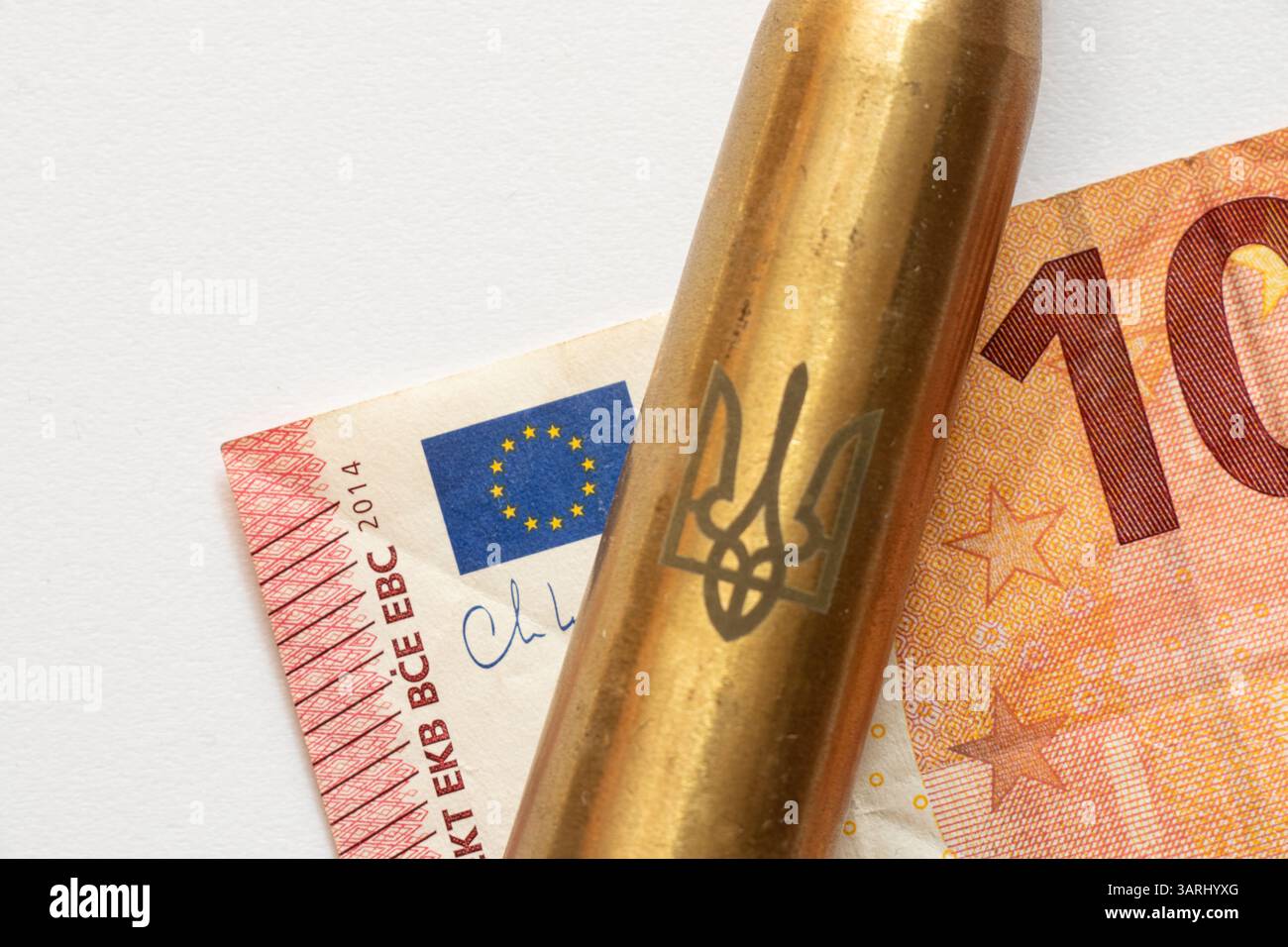 Un proiettile con lo stemma dell'Ucraina giace su una banconota da dieci euro su sfondo bianco, denaro per armi, acquisto di armi per l'Ucraina Foto Stock