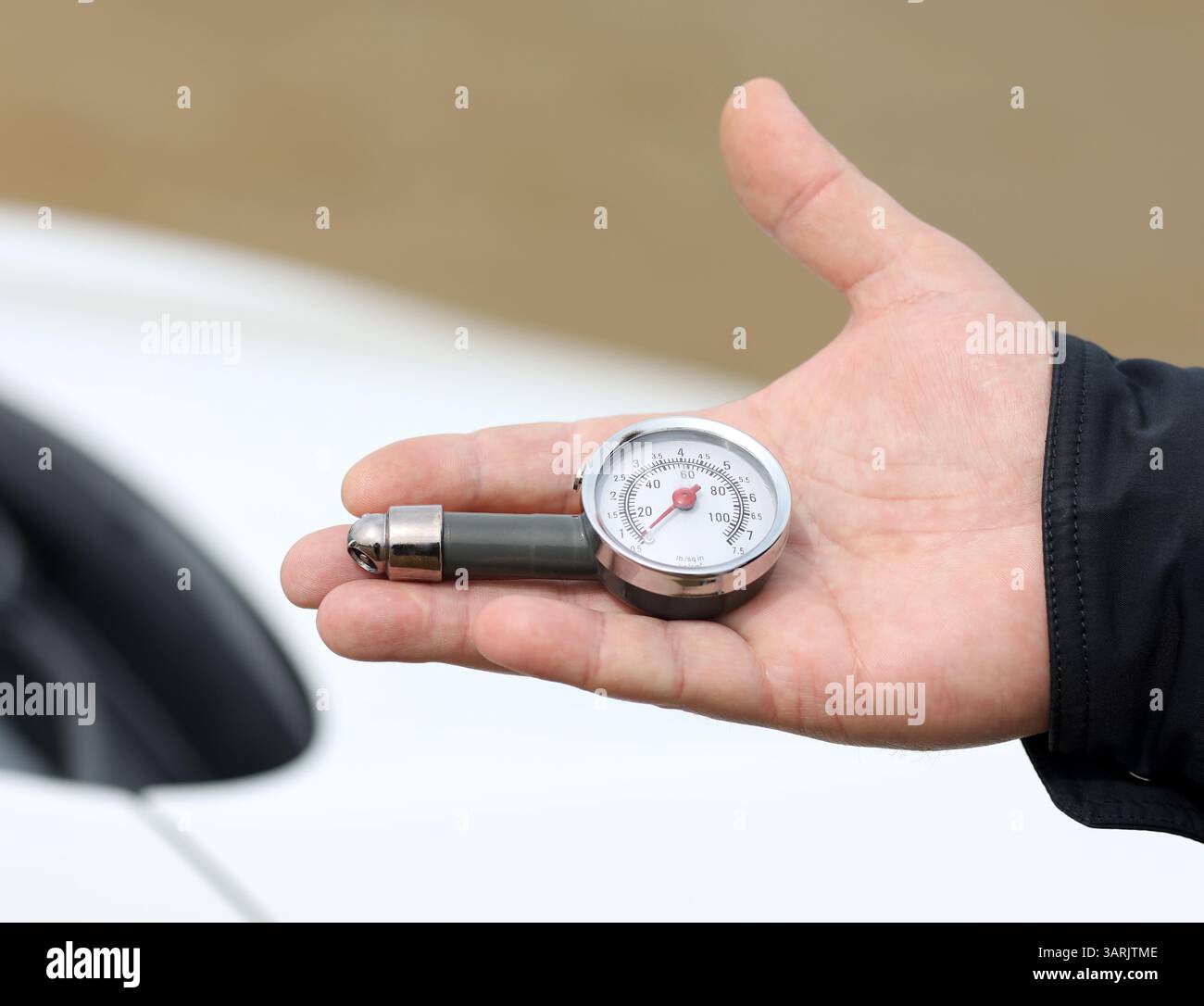 Perdita di una mano con un manometro analogico per pneumatici, con un quadrante chiaro che mostra i valori di psi e kPa, sullo sfondo di un veicolo bianco Foto Stock