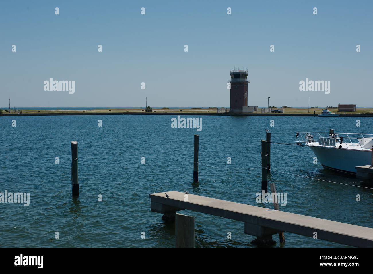 Vista panoramica della baia con porticciolo, panchina e torre di controllo sotto il cielo limpido. Vista sulla baia con porticciolo, barca parcheggiata, panchina e un posto lontano Foto Stock