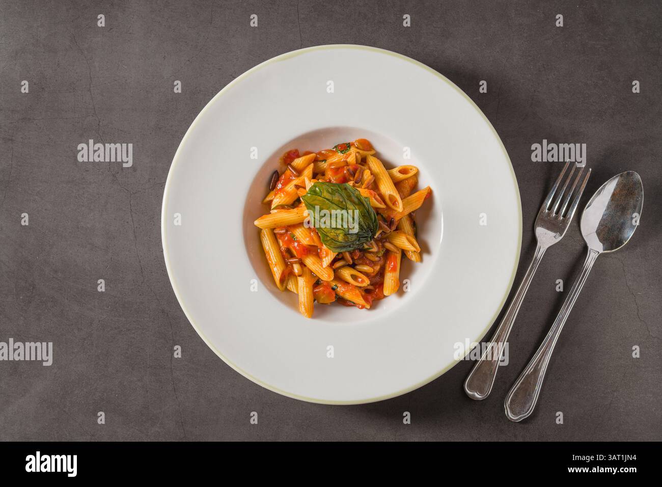 Penne alla arrabiata classica italiana con basilico e salsa su tavolo grigio scuro. Penne arrabbiata con salsa piccante Foto Stock