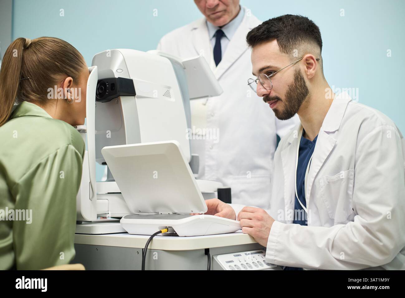 Donna sottoposta a un esame oculistico con un optometrista che utilizza apparecchiature mediche in ambiente clinico. Medico di alto livello che osserva la procedura in background Foto Stock