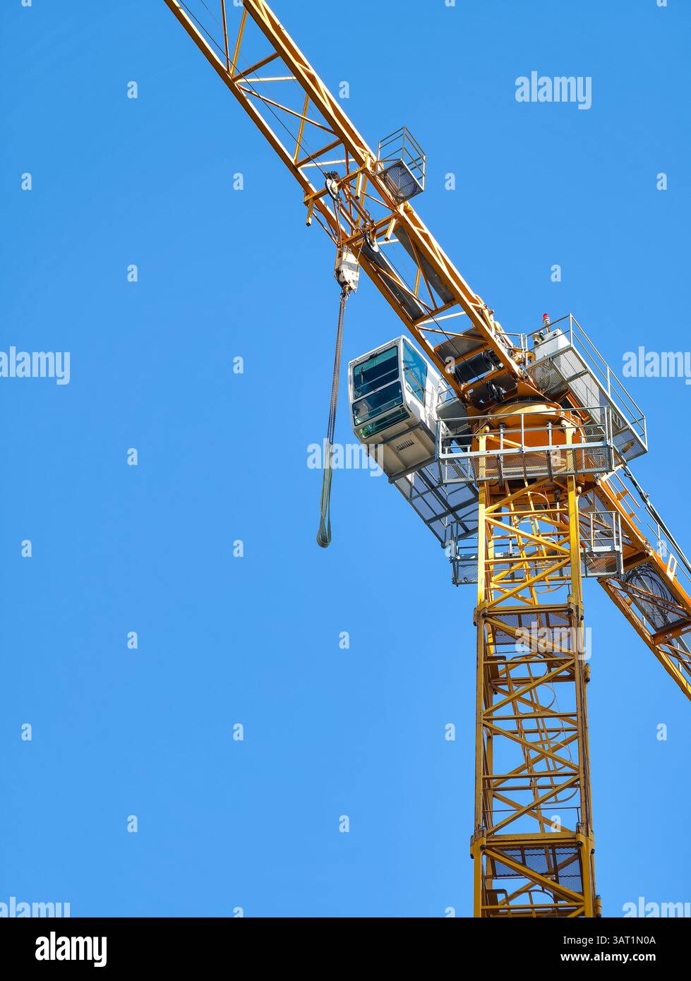 Gru a torre gialla brillante contro un cielo blu chiaro. Macchinari industriali utilizzati per il sollevamento di materiali nei cantieri edili. Ingegneria moderna Foto Stock