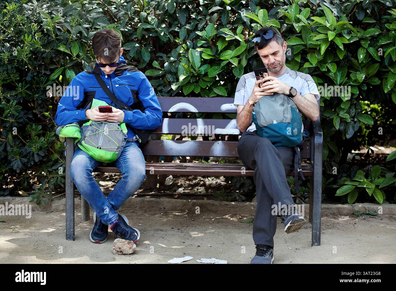 Due uomini seduti su una panchina incollati ai loro telefoni. Foto Stock