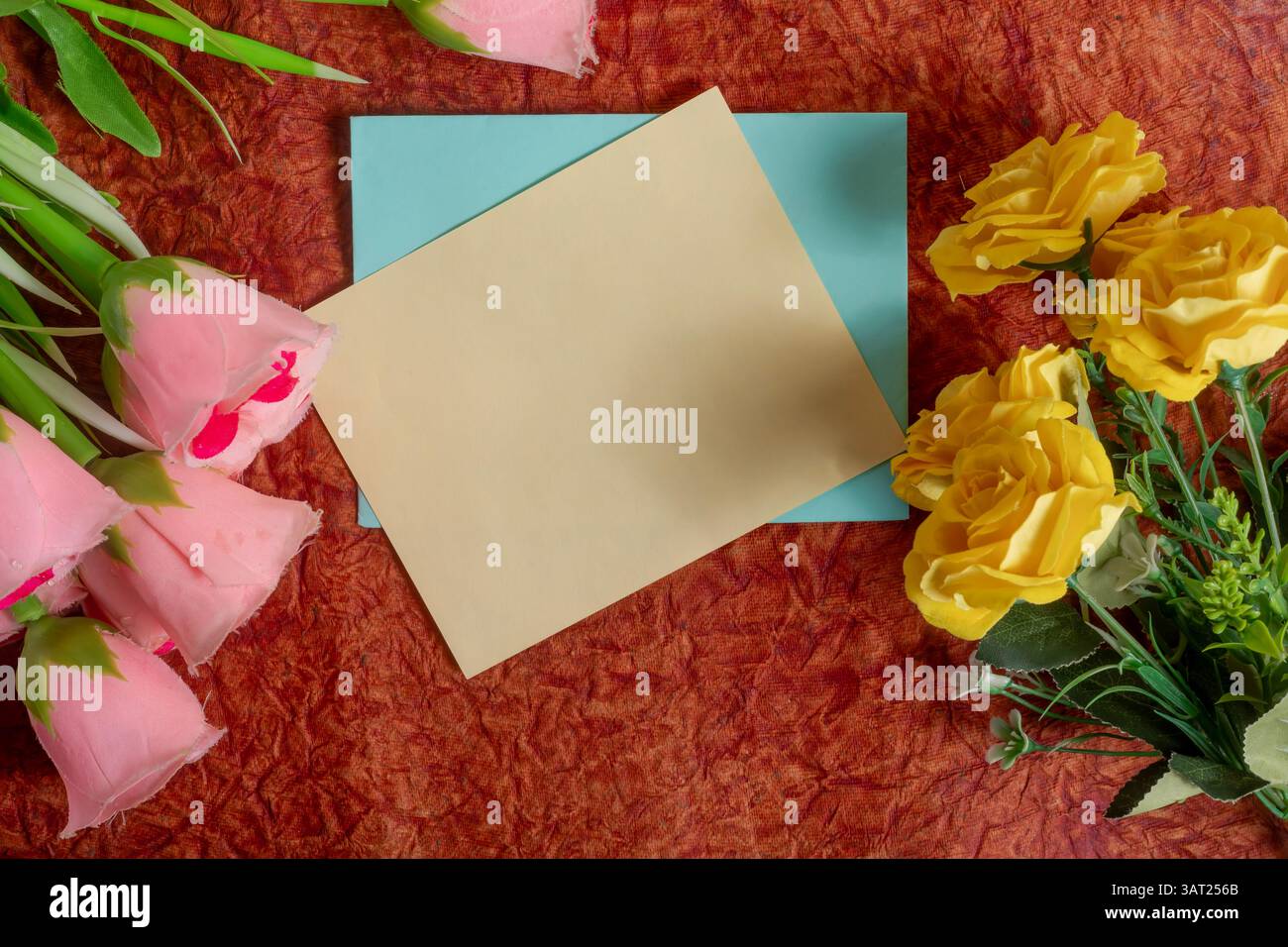 Una carta bianca posizionata su una superficie testurizzata circondata da fiori rosa e gialli fornisce una luce allegra e invitante per una varietà di occasioni. Foto Stock