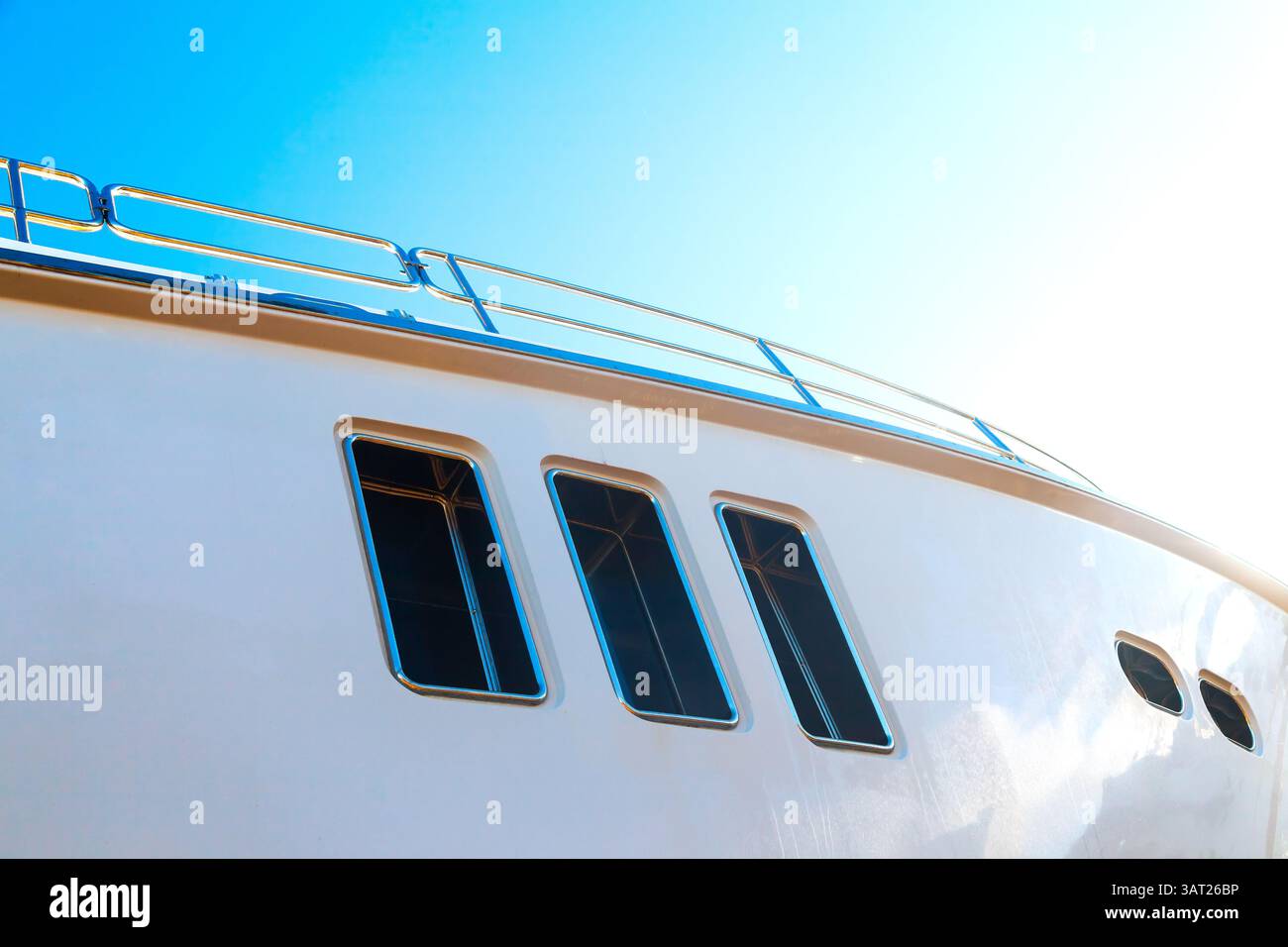 Lo scafo di un lussuoso yacht bianco a motore, con oblò sopra, contro il cielo blu e la luce del sole nell'angolo, vista dal basso. Foto Stock