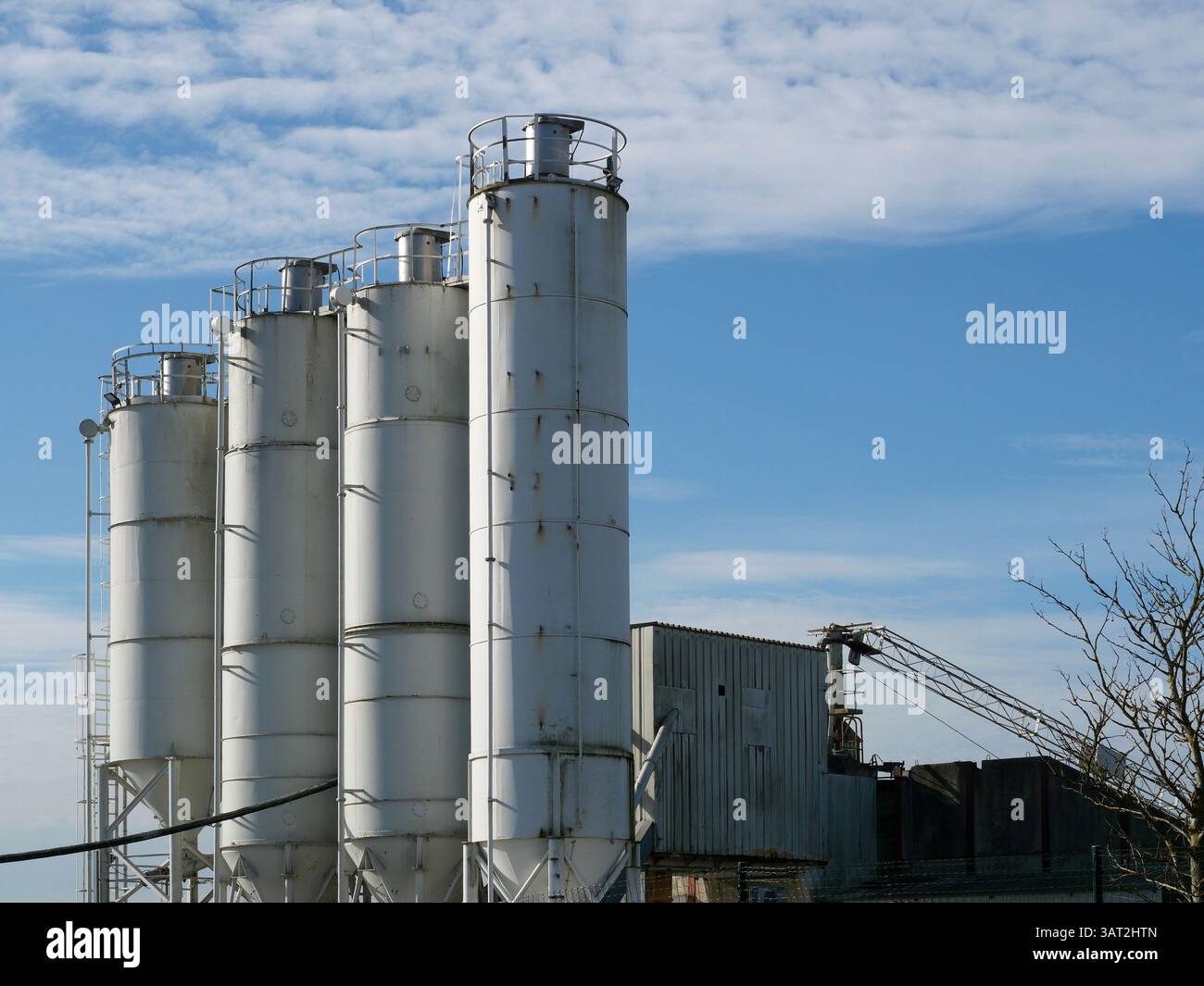 Più silos di una pianta di cemento si innalzano nel cielo. Impianto industriale in un'area commerciale, essenziale per i materiali da costruzione. Foto Stock