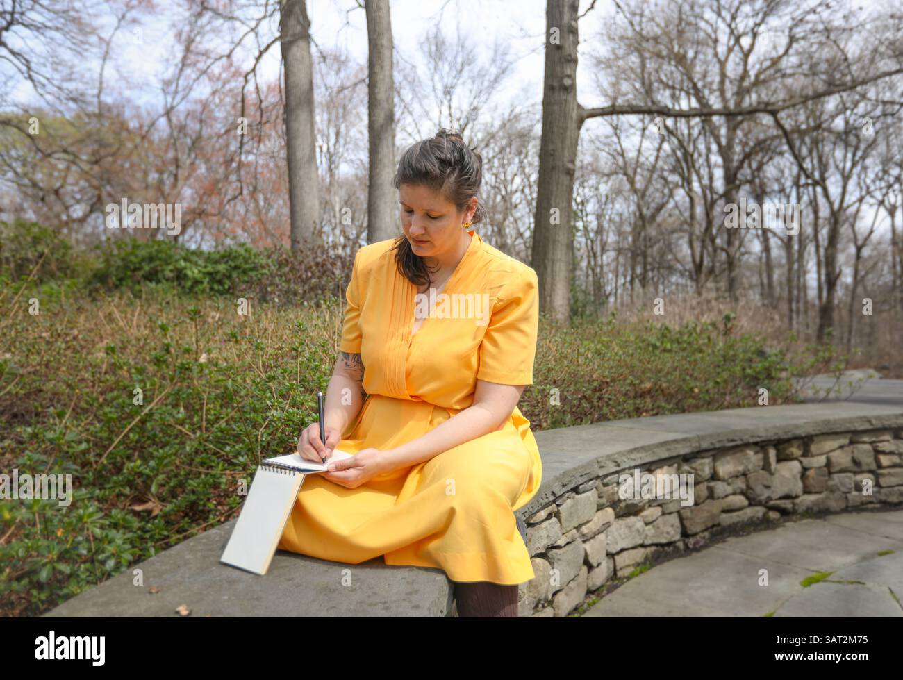 Donna con un abito Citrine seduto su una parete di roccia e disegna Foto Stock