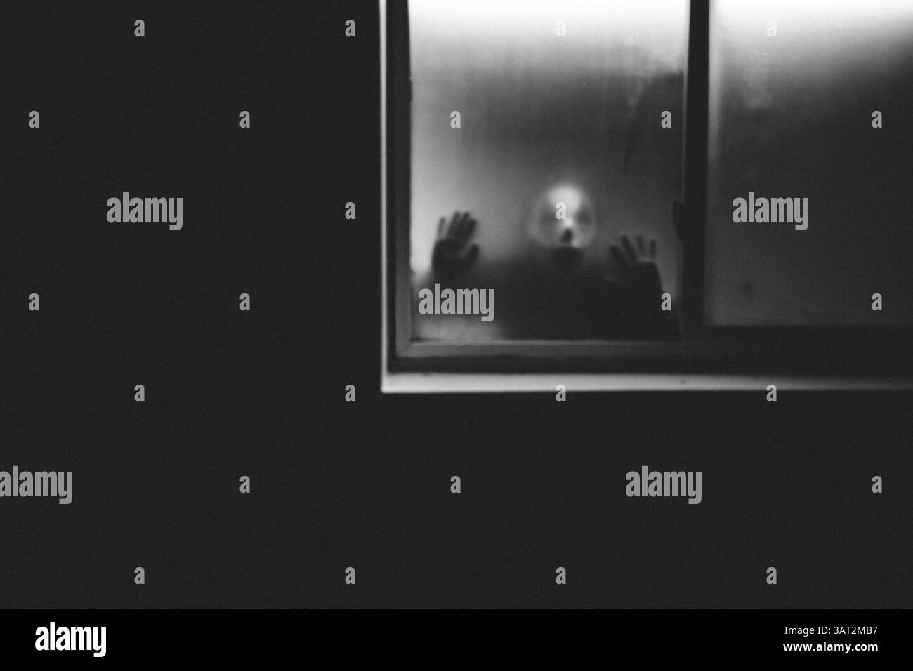 Il clown dell'orrore sbircia attraverso una finestra nebbiosa di casa buia di notte Foto Stock