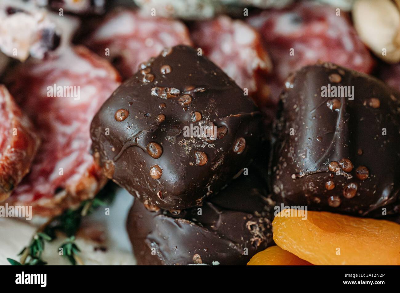 Primo piano di prelibatezze al cioccolato fondente accanto a salame e albicocche secche. Foto Stock