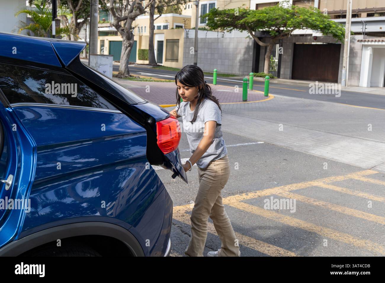 Un adolescente sta tirando un'auto blu fuori da un parcheggio. L'auto è parcheggiata in parecchio con qualche altra auto Foto Stock Un adolescente sta tirando un'auto blu fuori da un parcheggio. L'auto è parcheggiata in parecchio con qualche altra auto Foto Stock
