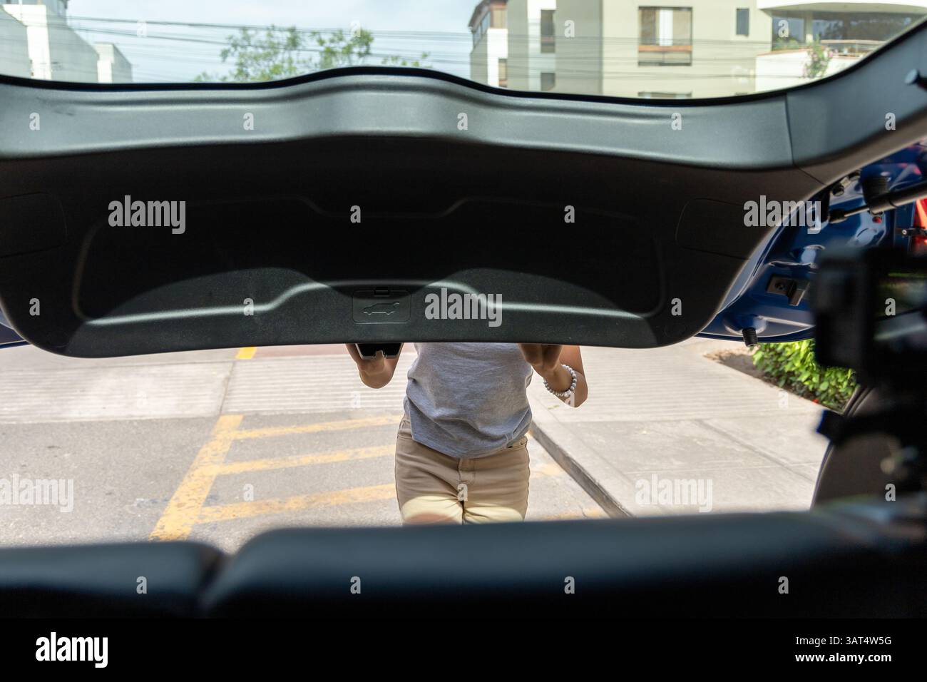 Un adolescente è in piedi davanti a un'auto con un bagagliaio nero. Sta tenendo un cellulare in mano Foto Stock Un adolescente è in piedi davanti a un'auto con un bagagliaio nero. Sta tenendo un cellulare in mano Foto Stock