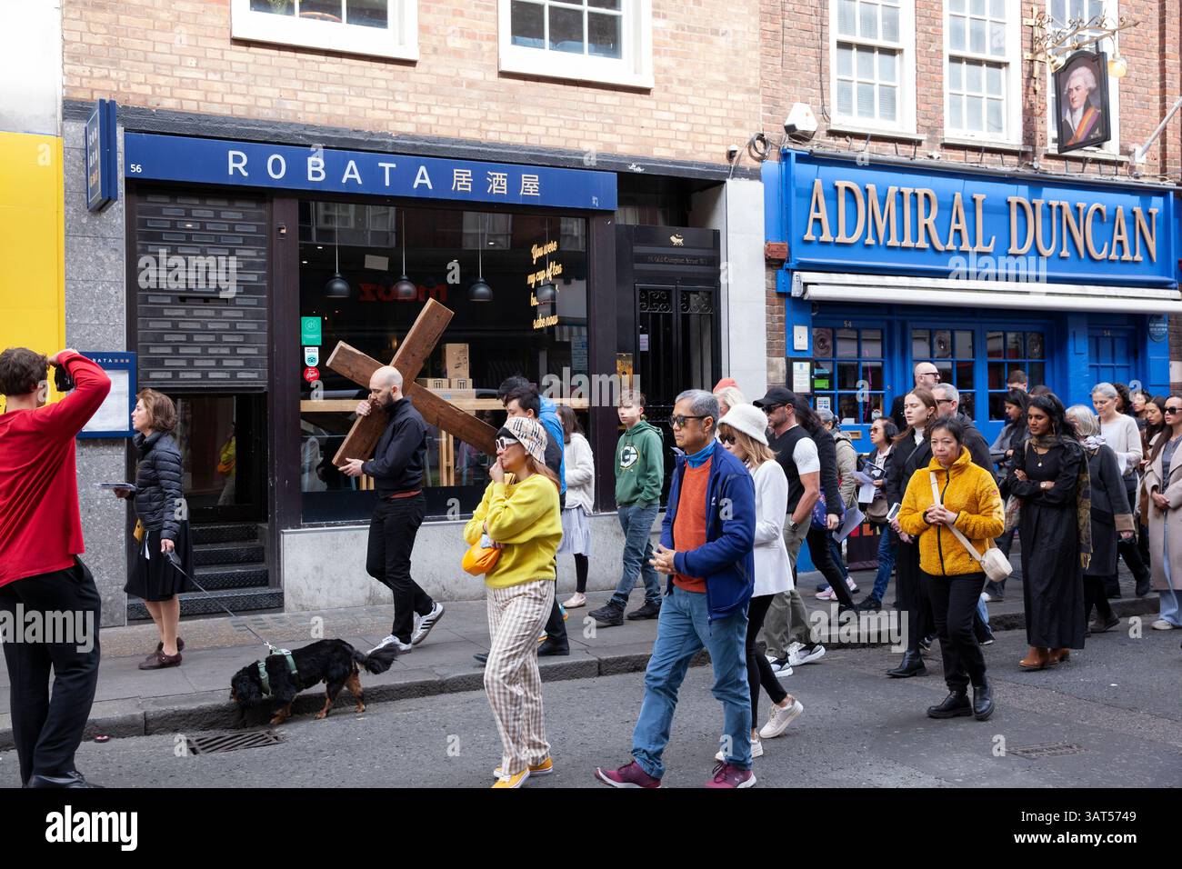 Londra, Regno Unito. 18 aprile 2025. In occasione del venerdì Santo, la Chiesa cattolica di San Patrizio ha tenuto una processione per segnare le stazioni della Croce, portando un crocifisso in legno intorno alle vicine strade di Soho. Il parroco padre Alexander Sherbrooke guidò la congregazione multiculturale in preghiere per segnare ciascuno dei passi del cammino di Gesù, e i fedeli cantarono mentre camminavano. Crediti: Anna Watson/Alamy Live News Foto Stock