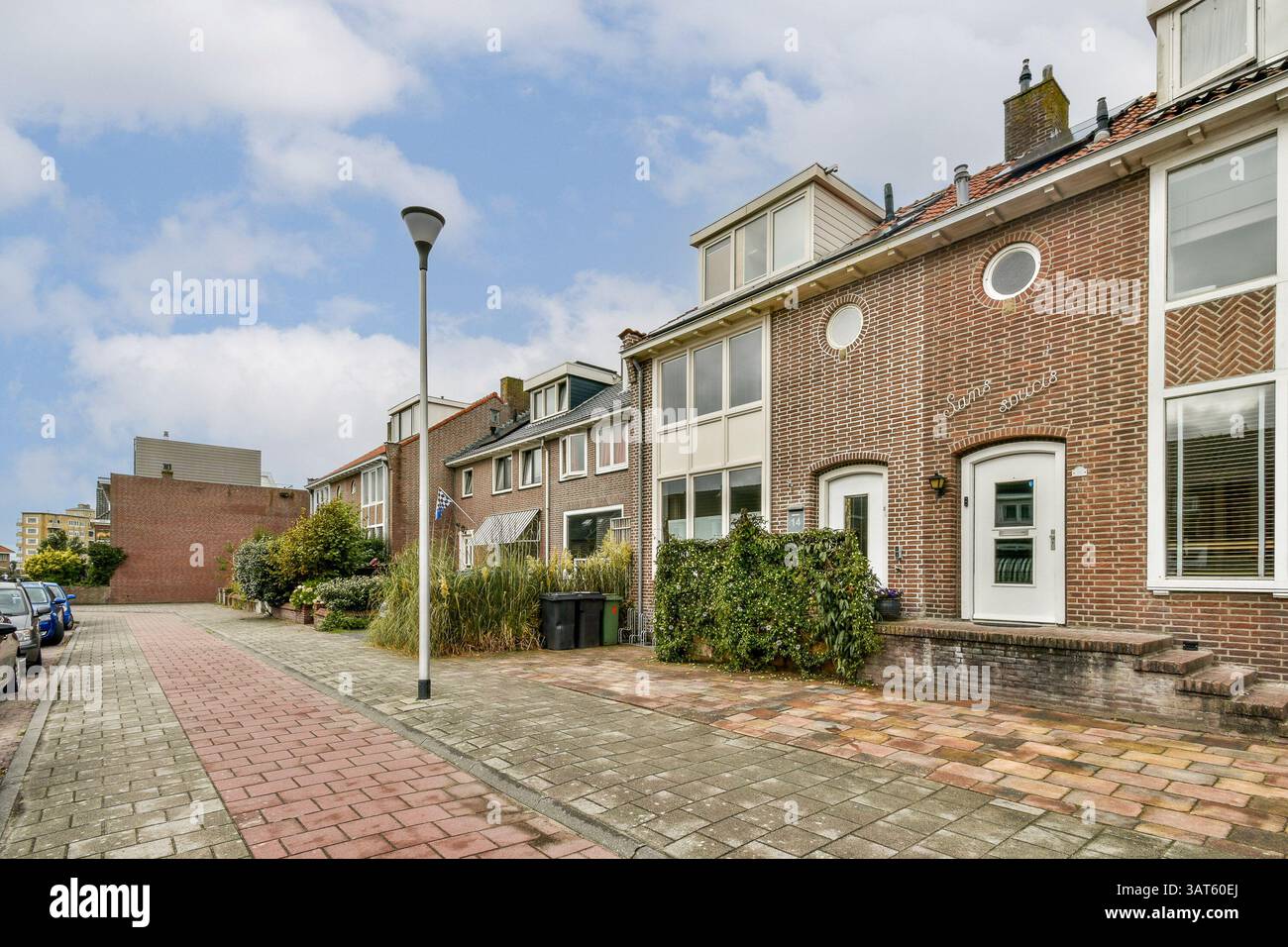 Una pittoresca strada urbana caratterizzata da case in mattoni, giardini ben tenuti e sentieri acciottolati. I cieli luminosi migliorano l'atmosfera serena e invitano a passeggiare. Foto Stock