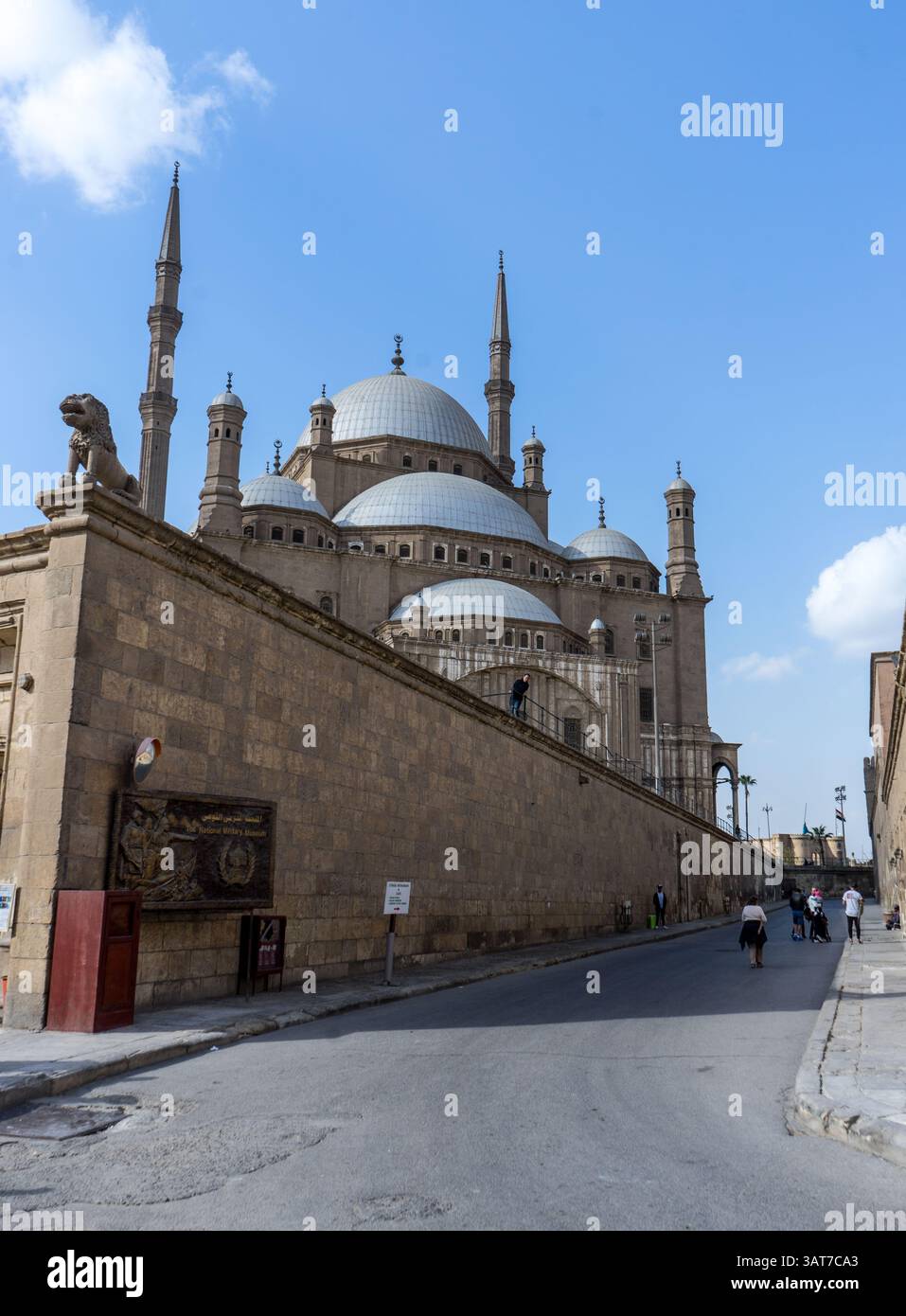 Una moschea storica con grandi cupole e alti minareti, adagiata su un cielo azzurro. La moschea è circondata da un muro di pietra, con la gente che cammina vicino Foto Stock