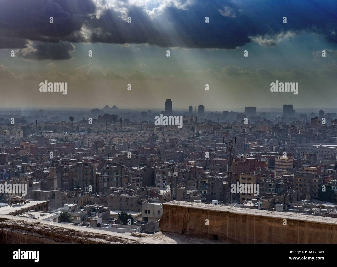 Una vista panoramica del Cairo, in Egitto, che mostra un vasto paesaggio urbano sotto un cielo spettacolare con raggi di luce del sole che si infrangono attraverso le nuvole. Gli iconi Foto Stock