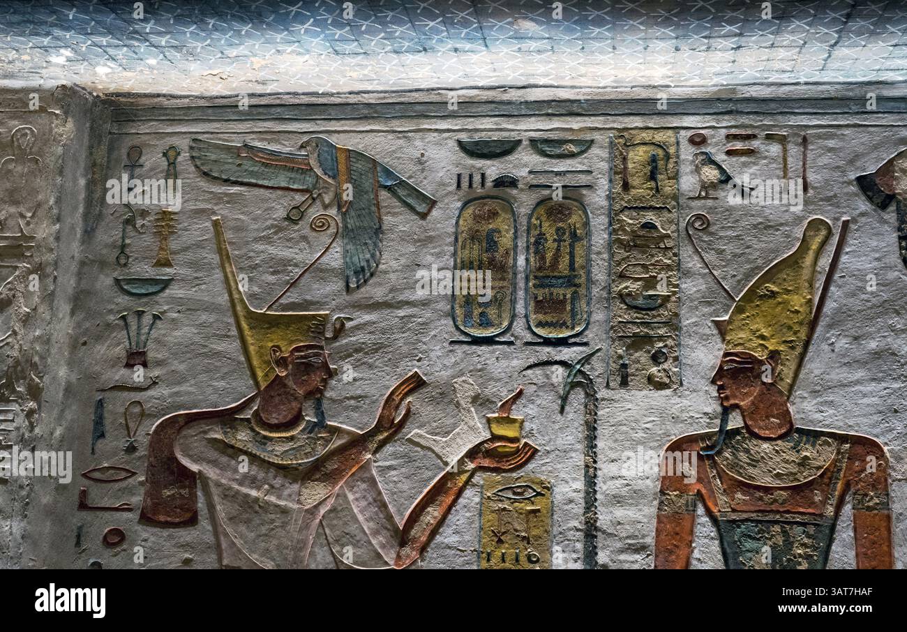 Antico rilievo murale egizio raffigurante due figure in copricapi elaborati, impegnati in un rituale o offerta. Geroglifici e simboli li circondano, s. Foto Stock