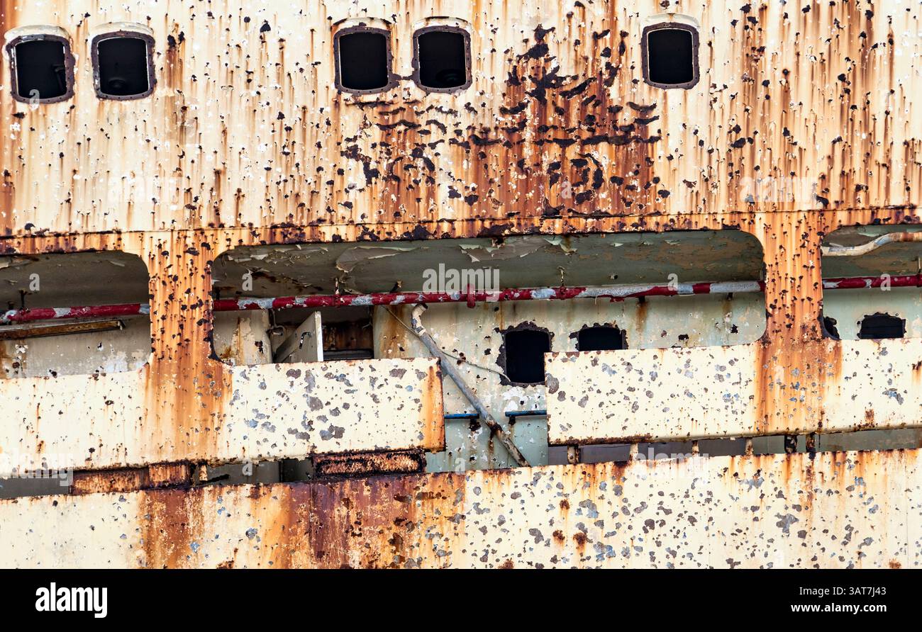 Primo piano di uno scafo arrugginito e intempestivo con vernice e oblò. Foto Stock