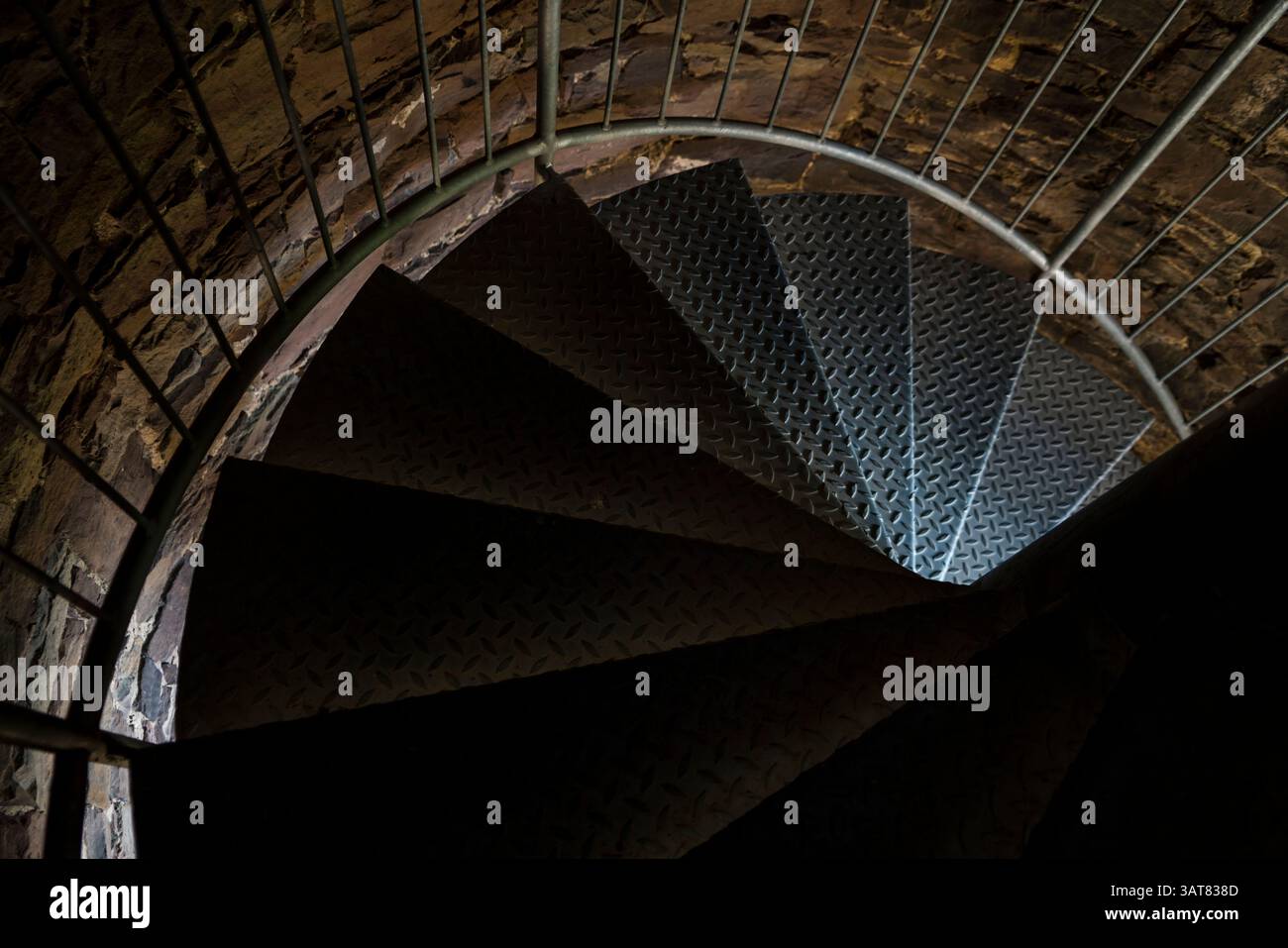I gradini della vecchia scala a spirale in metallo scompaiono nel buio Foto Stock