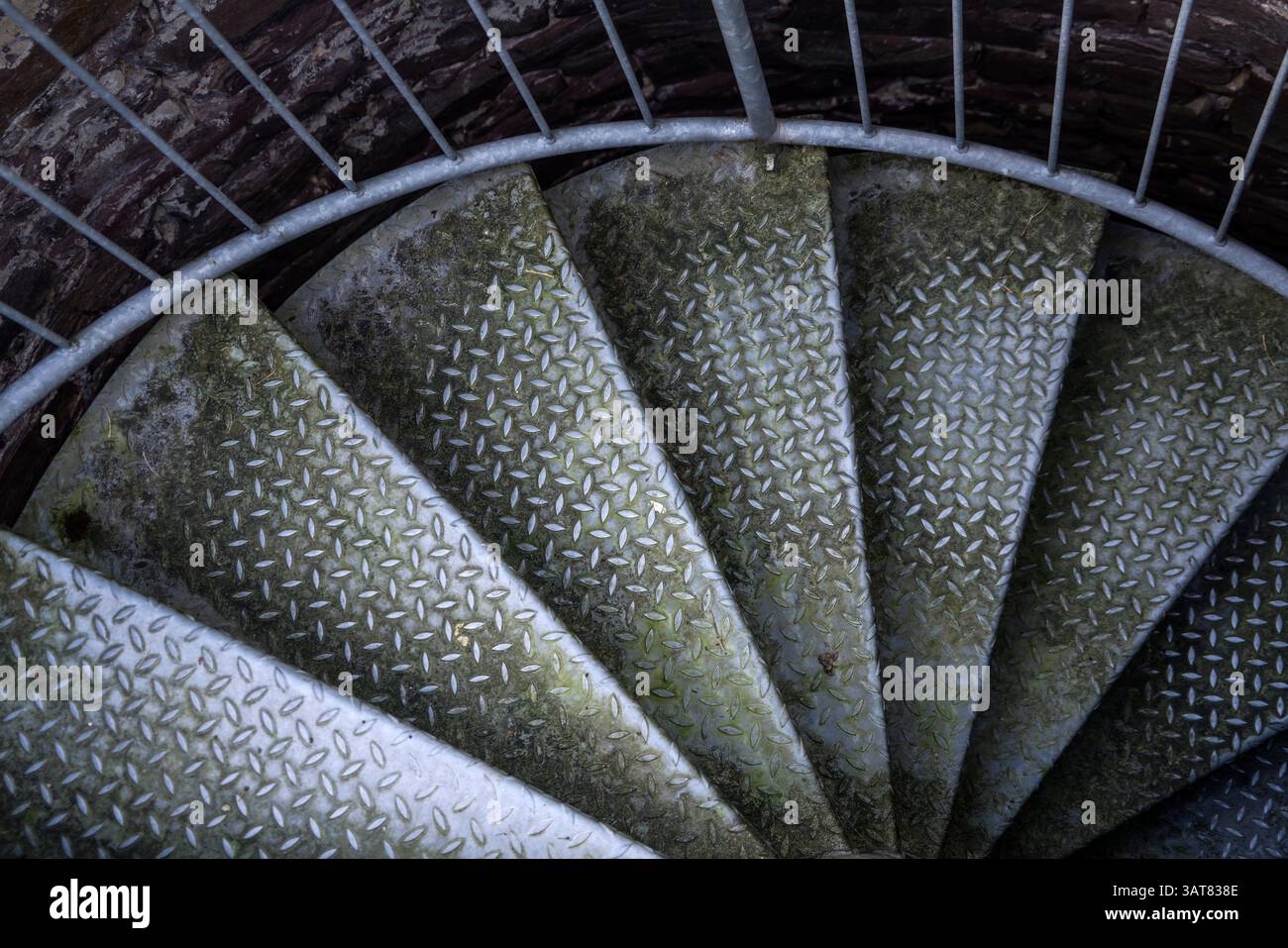 I gradini della vecchia scala a spirale in metallo scompaiono nel buio Foto Stock