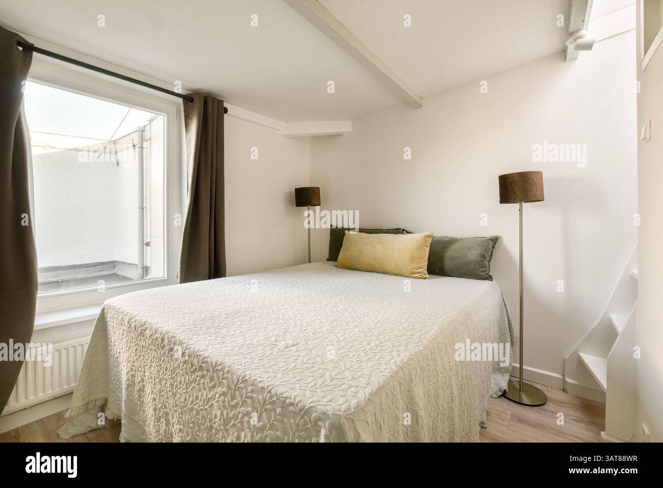 Una camera da letto tranquilla con un comodo letto e una grande finestra che invita alla luce naturale, creando un'atmosfera calda e invitante. Foto Stock