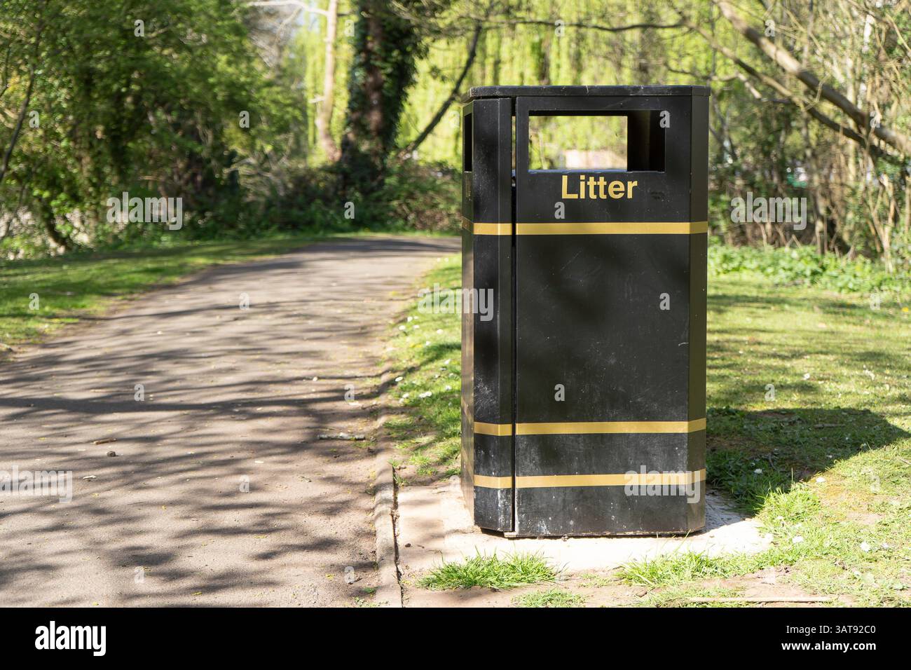 Cestino nero in un parco verde nel Regno Unito. Il cestino è collocato vicino a un sentiero asfaltato che attraversa il parco Foto Stock