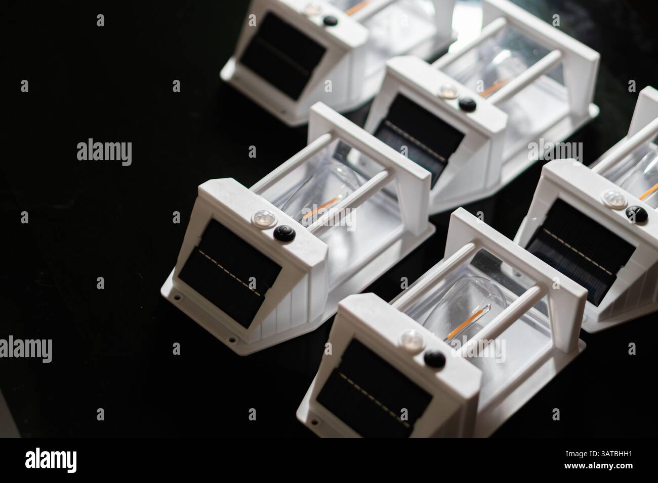 Vista ravvicinata di diversi dispositivi a energia solare bianchi disposti in fila su una superficie scura. Ogni dispositivo è dotato di uno scomparto trasparente e di un fotovoltaico Foto Stock